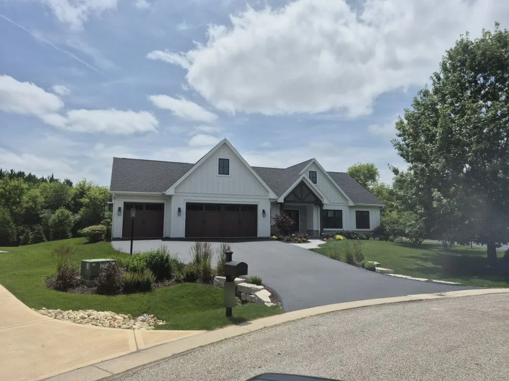 Modern farmhouse with white vertical siding, dark shingle roof and timber gable entry